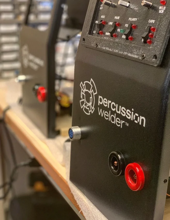 Angled view of the Percussion Welder 858 front panel and output jacks with a second unit behind it on the bench