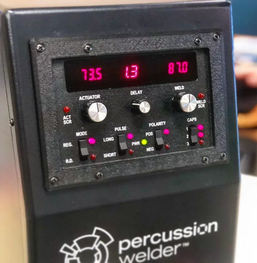 Close-up of the Percussion Welder 858 front panel: red readouts, actuator, delay and weld knobs, mode, pulse, polarity and caps switches