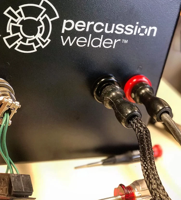Close-up of the Percussion Welder logo above the black and red weld output jacks with braided cables connected