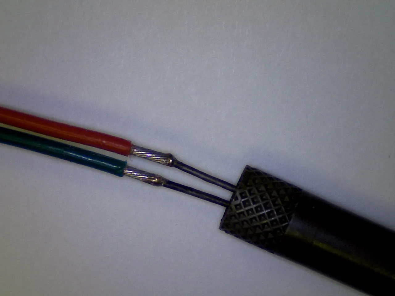 Red and green wires joined and held by tweezers, magnified