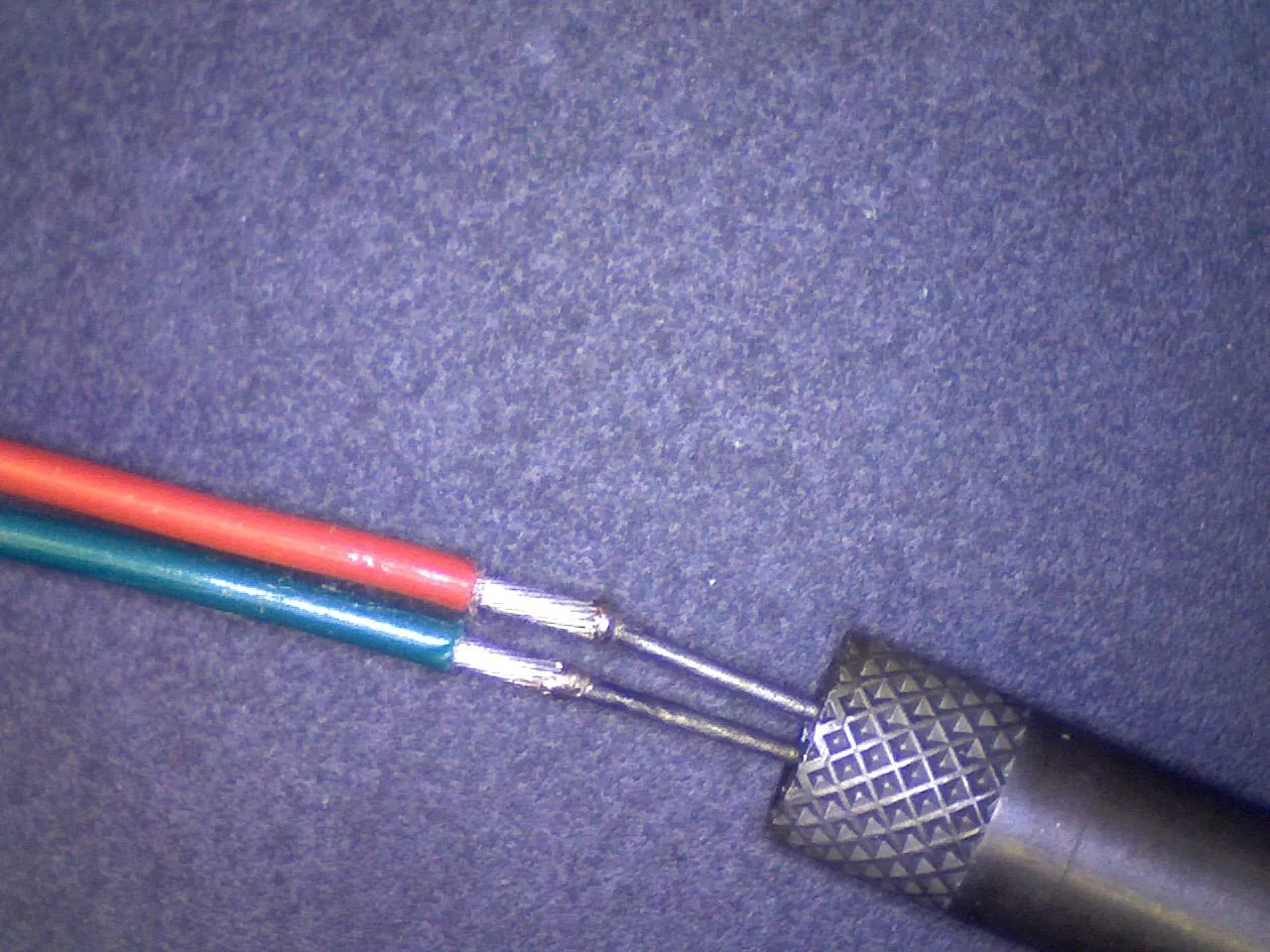 Red and green insulated wires joined with tweezers, magnified view