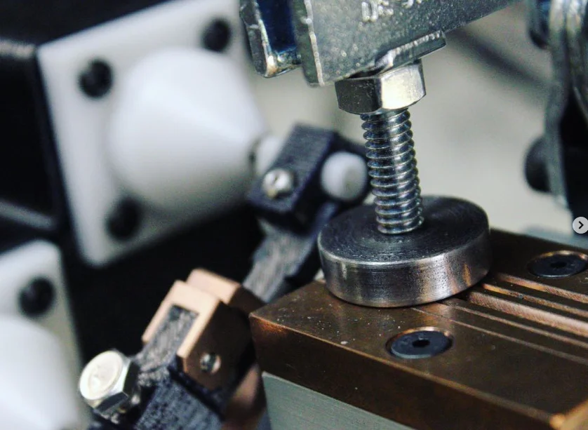 Close-up of the 726 fixture: a clamp screw and steel pad over a grooved copper block, with a white cone and wire holder at left
