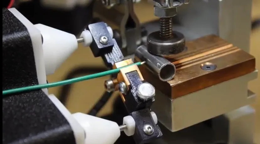 Green wire clamped between white electrode cones on the bench fixture