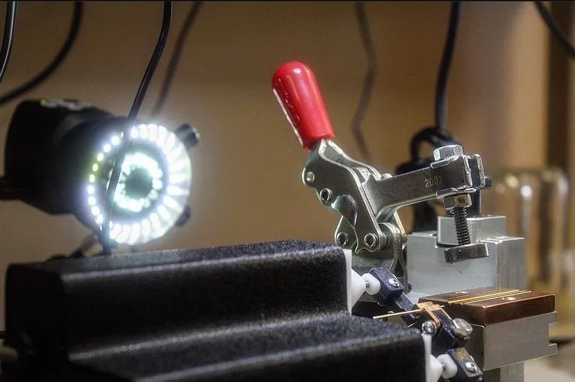 Bench fixture with red toggle clamp and a ring light above the weld area