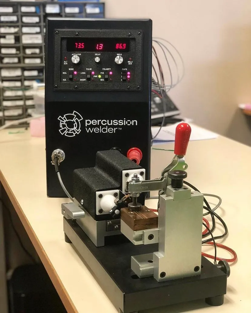 Percussion welder and bench fixture with red toggle clamp on a workbench