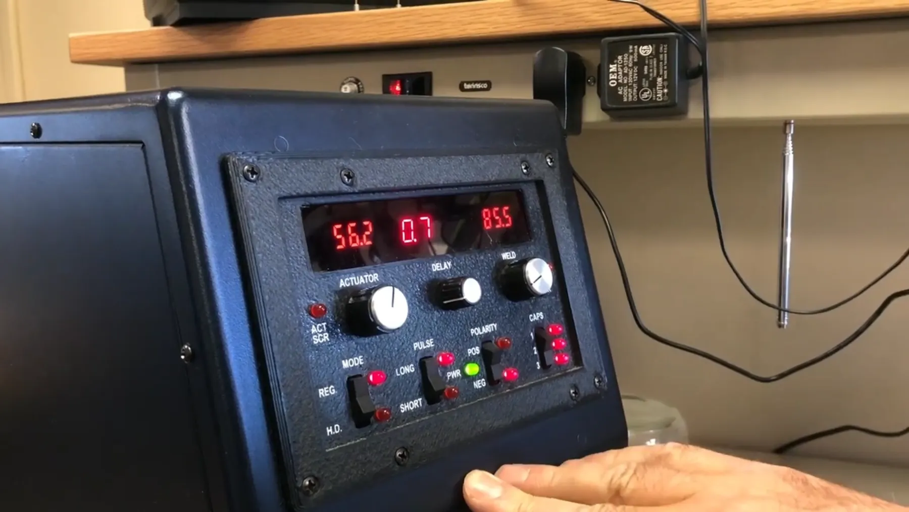 Hands operating the front panel of the percussion welder with red LED readouts