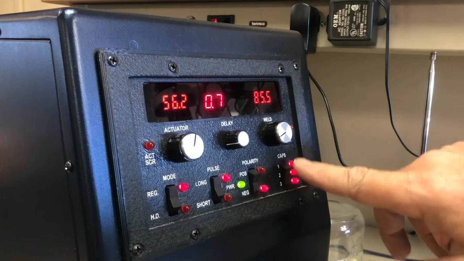 Finger pressing a control on the percussion welder front panel