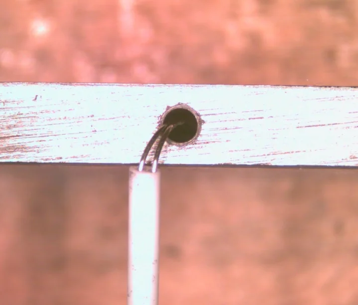 Microscope view of a thermocouple wire pair welded at the bottom of a 1/16 inch hole drilled in the side of a stainless steel plate, with a white ceramic insulator below