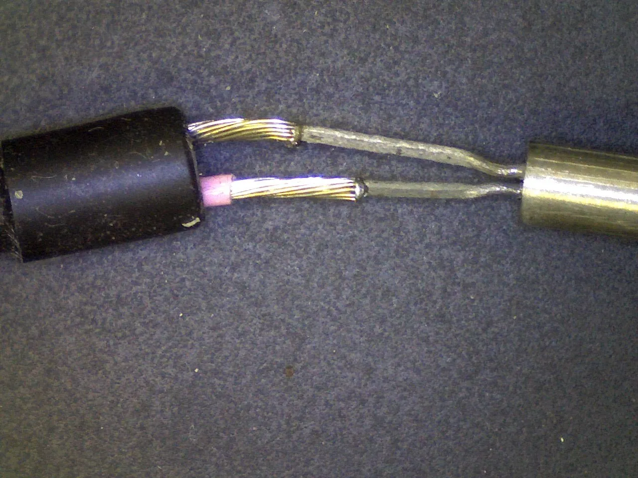 Two stranded thermocouple wires being joined with a pink glow at the tip