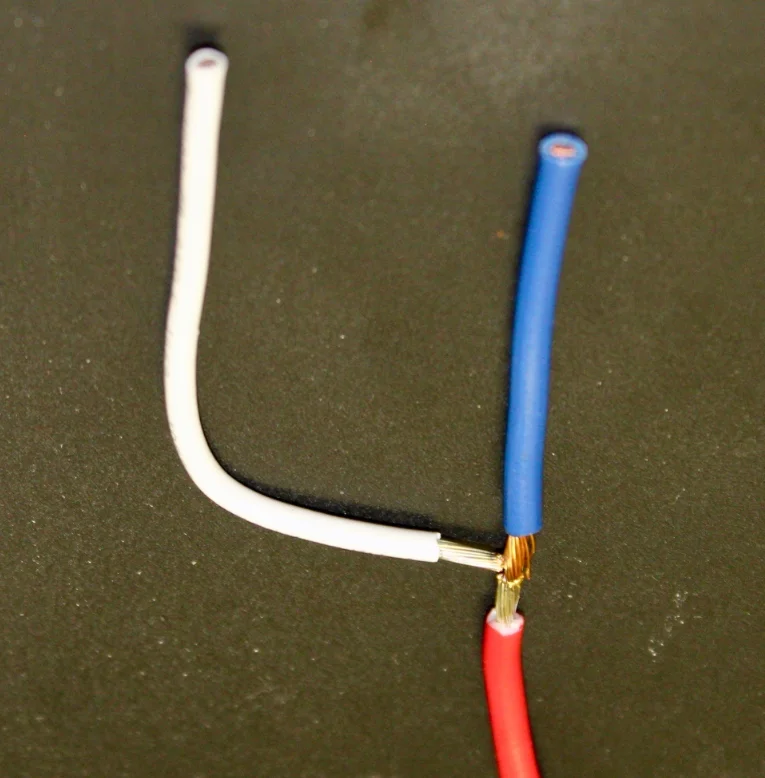 Three insulated stranded wires, white, blue and red, joined together at a single welded junction on a dark surface