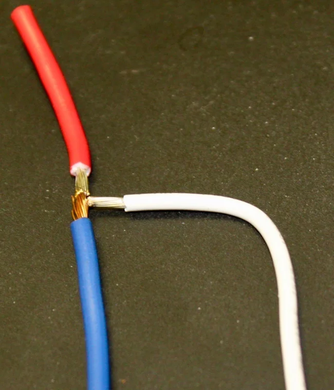 Red, blue and white insulated wires welded together at one junction, with the stripped strands visible