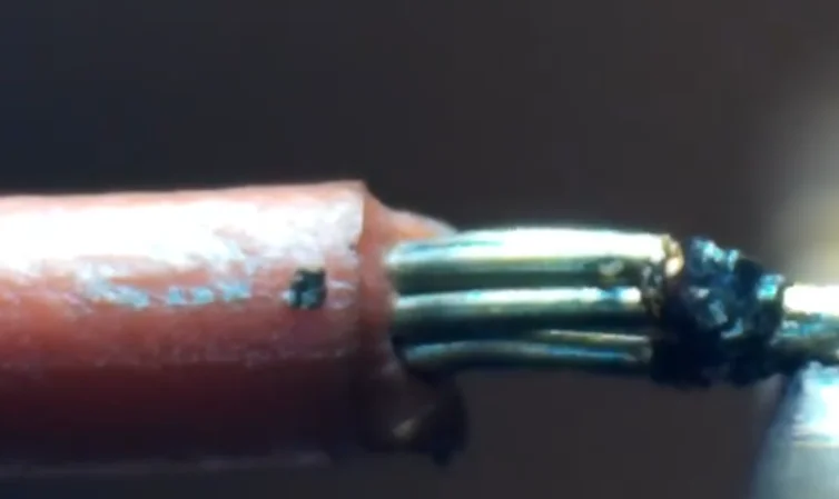 Microscope close-up of stranded wire welded at the end, with insulation at left and a dark fused tip at right