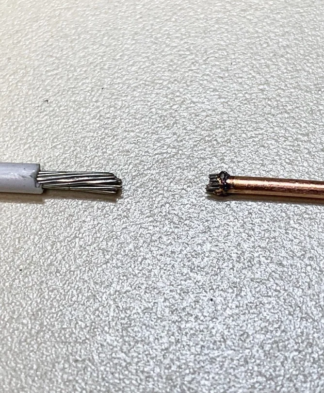 Two wire ends on a work surface: a stranded wire with white insulation at left and a copper wire with a scorched end at right