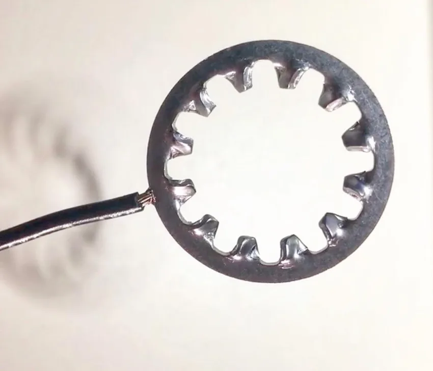 Black insulated wire welded to the edge of a serrated lock washer, held up against a plain background